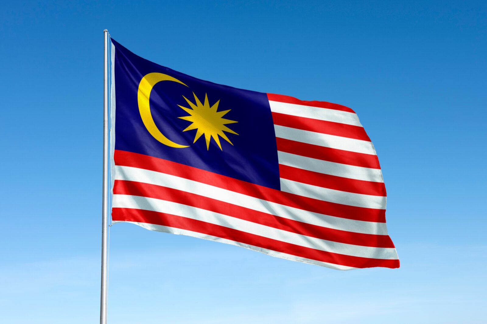Malaysian flag waving on a flagpole against a blue sky