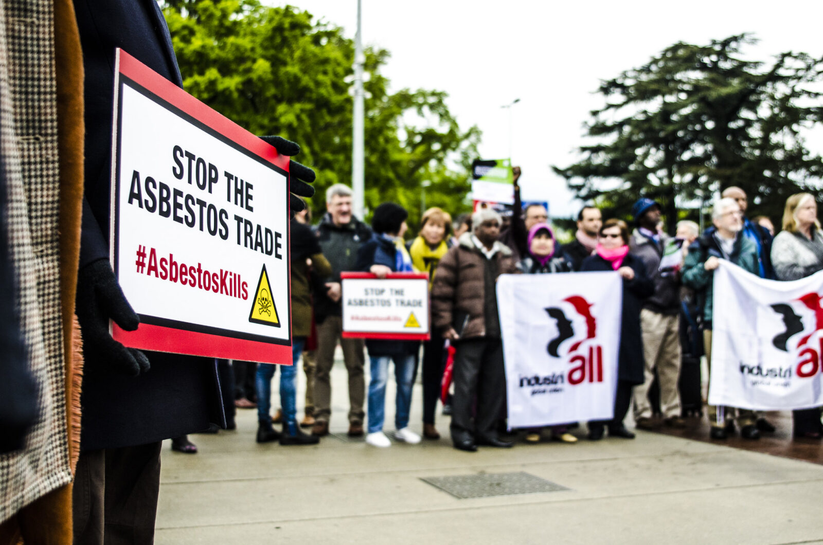 Protesters outside the UN in Geneva holding signs reading "Stop the asbestos trade – #Asbestoskills" alongside IndustriALL Global Union banners.