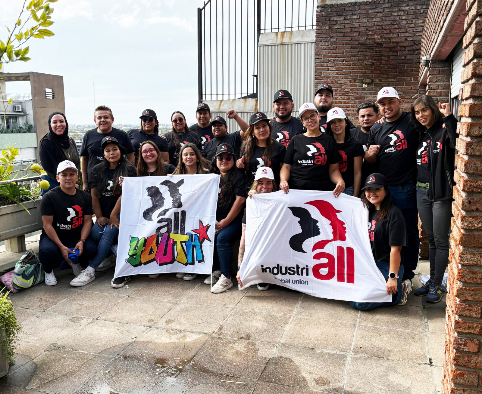 Grupo de jóvenes con camisetas negras de IndustriALL posando con banderas en una terraza en Montevideo, Uruguay