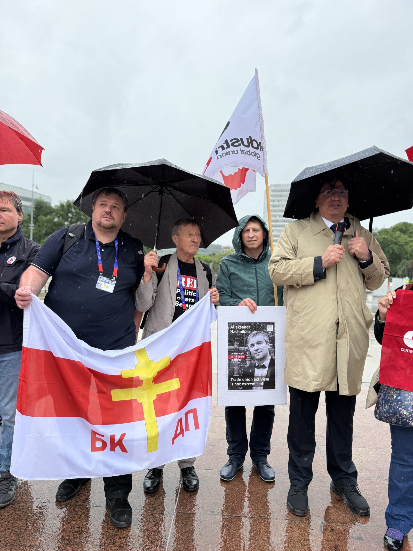 Trade union activists hold a BKDP flag and a poster of imprisoned unionist Aliaksandr Hashnikau at a solidarity demonstration outside the UN Palace of Nations, Geneva