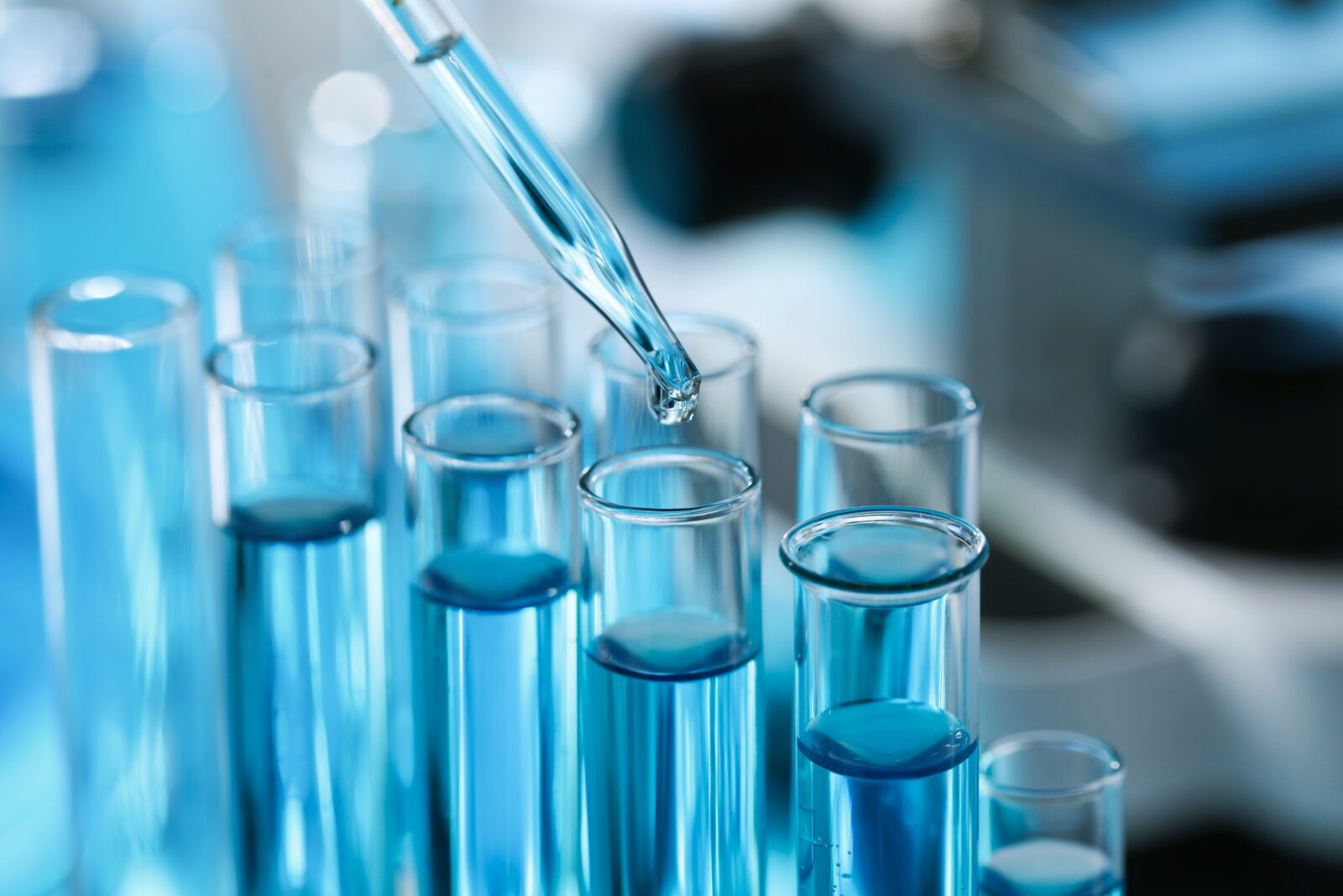 A pipette dropping liquid into a row of glass test tubes filled with blue liquid in a laboratory setting