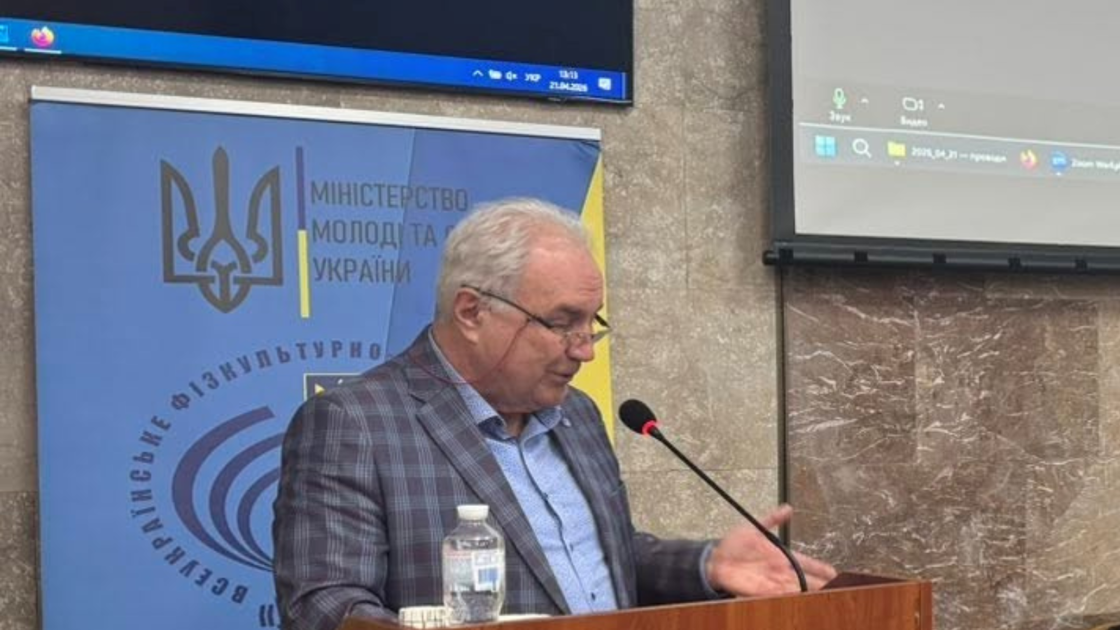 Yarema Zhuhaievych speaking at a podium with a microphone, in front of a Ukrainian ministry of youth and sport banner.