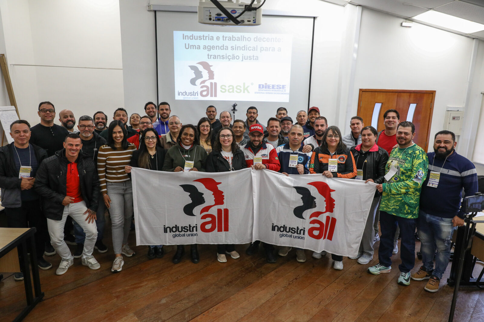Participantes del Seminario Sectorial de Movilidad del Proyecto SASK posan con banderas de IndustriALL Global Union durante una foto grupal en Brasil.