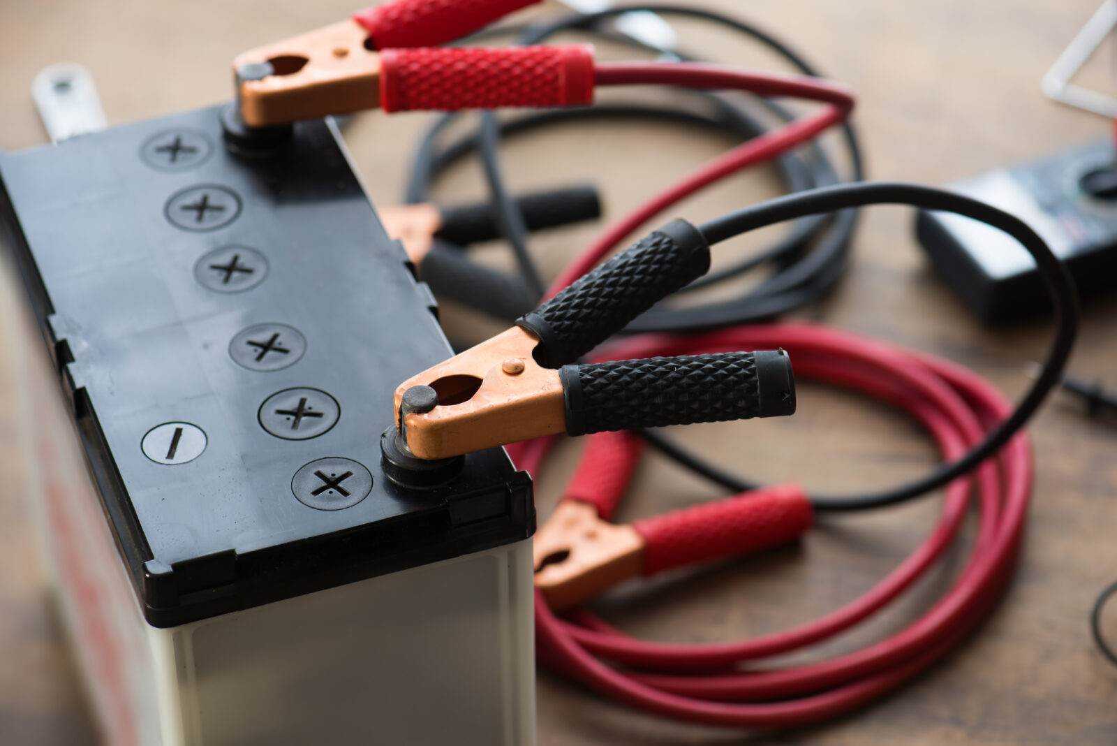 Car battery with jumper cable clamps attached to terminals