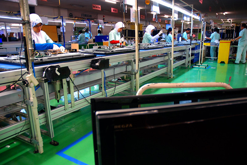 Workers in uniforms and headscarves assembling electronic components on a factory production line in Cikarang, Indonesia.
