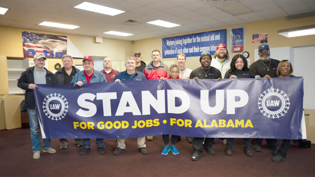 Trabajadores de la planta de Mercedes-Benz en Tuscaloosa, Alabama, sostienen una pancarta de la UAW con la inscripción «Stand up for good jobs, for Alabama»