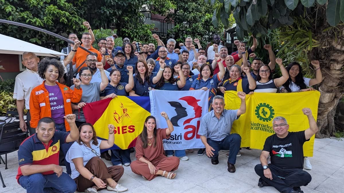 Trade union delegates raise their fists for a group photo at the regional energy sector meeting in San Salvador, holding SIES and IndustriALL flags.