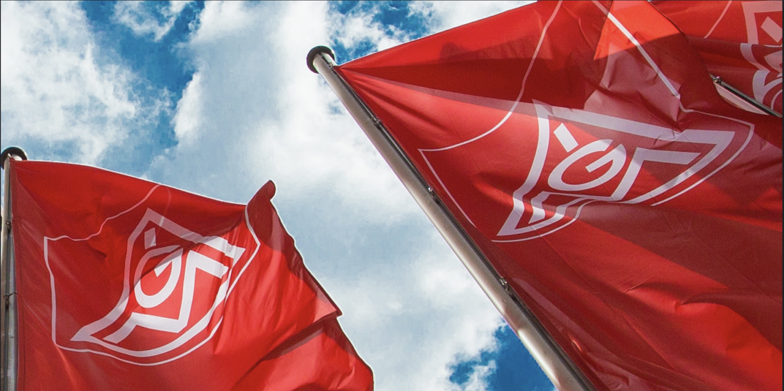 Red IG Metall union flags with white logos billowing against blue sky