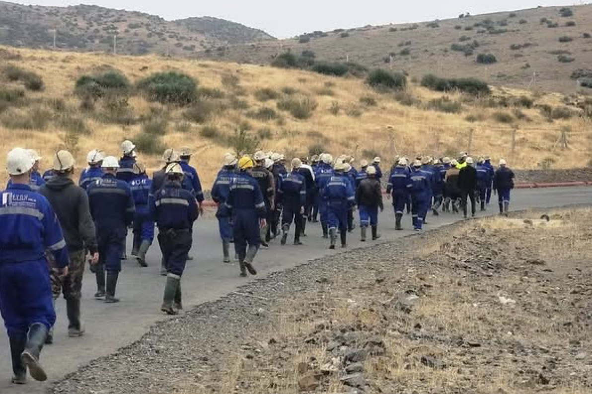 Miners in blue overalls and hard hats marching along a road through dry hills near M'rirt, Morocco, in protest after a fatal mine explosion.