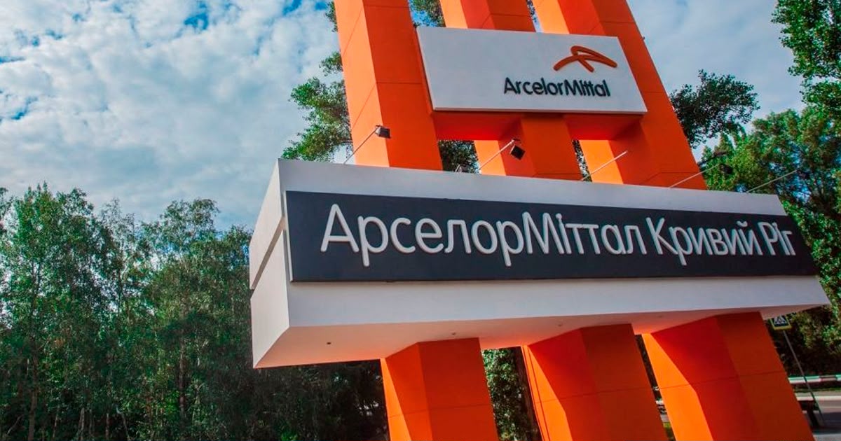 Orange and white sign with the ArcelorMittal logo and the name ArcelorMittal Kryvyi Rih in Ukrainian, surrounded by trees