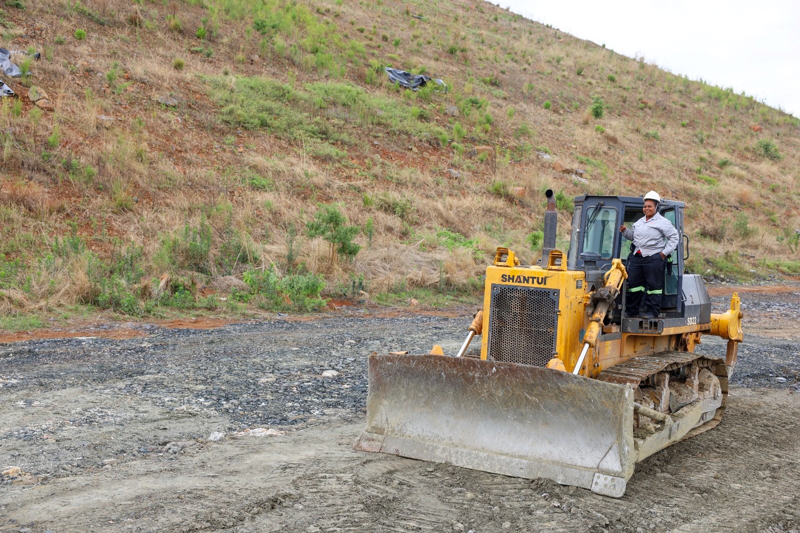 Woman in hard hat and overalls standing on a yellow bulldozer at an open-pit mine site in Zimbabwe