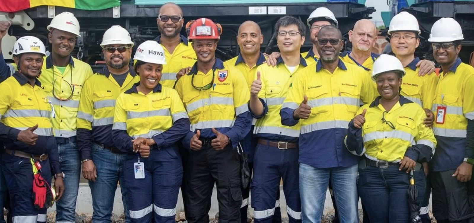Group of Simandou mine workers in yellow and navy Rio Tinto/Simfer high-visibility uniforms and hard hats, giving thumbs up, Guinea