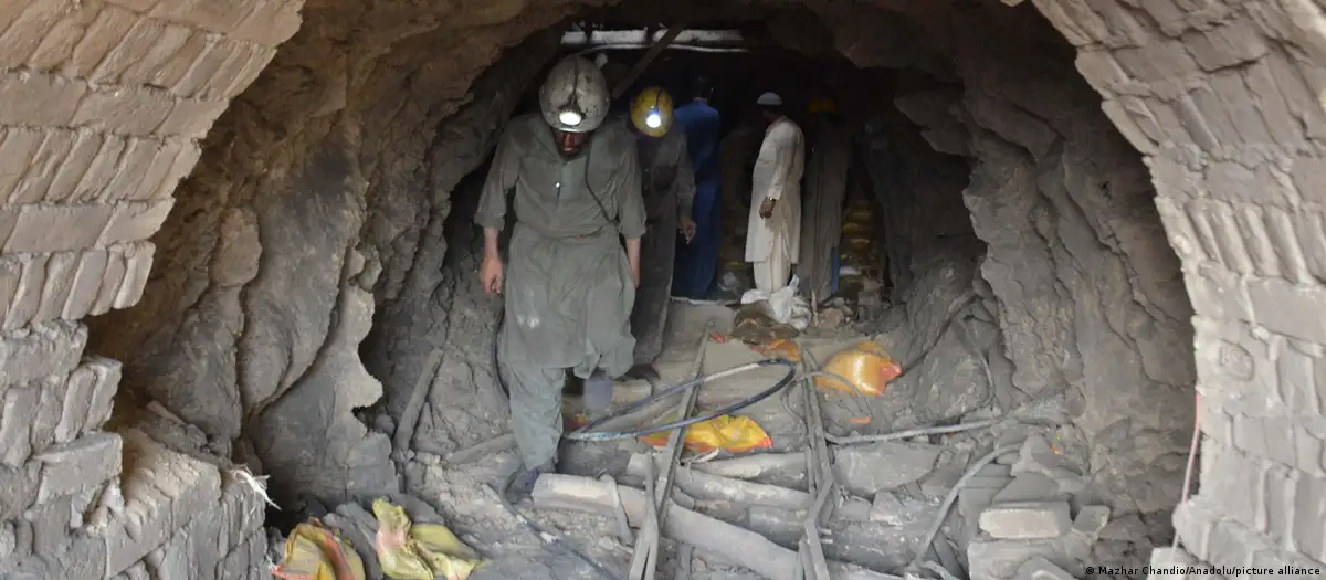 Miners in helmets with headlamps walk through a narrow brick-lined mine tunnel in Pakistan