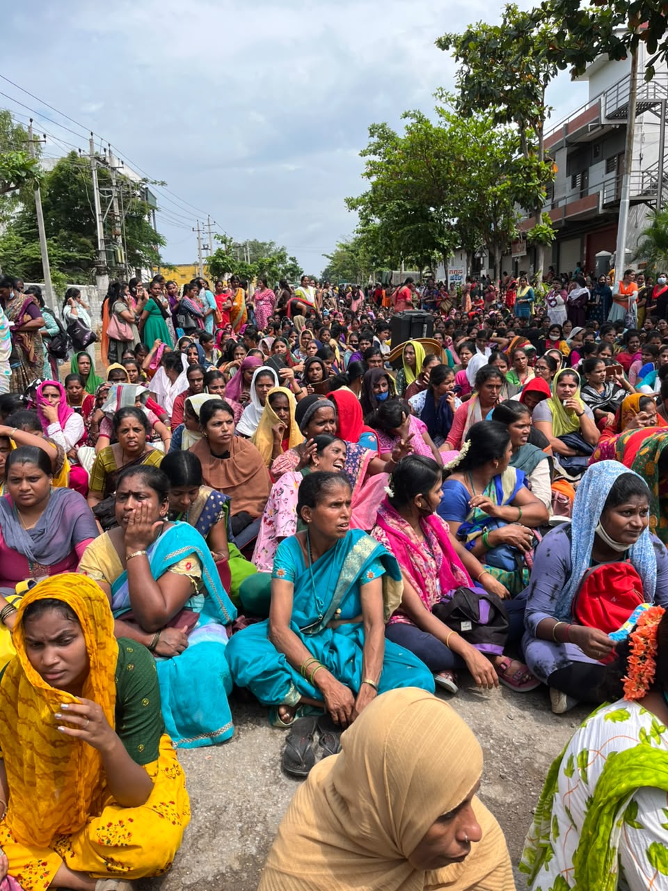 Hundreds of women garment workers sitting on a road in protest, stretching far into the distance.