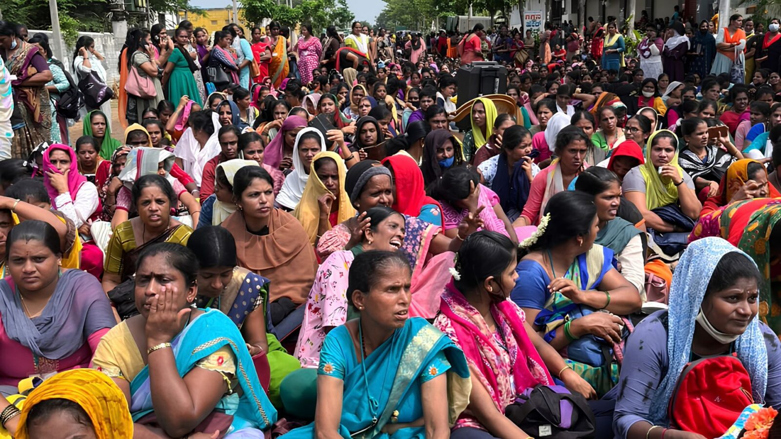 Hundreds of women garment workers sitting on a road in protest, stretching far into the distance.