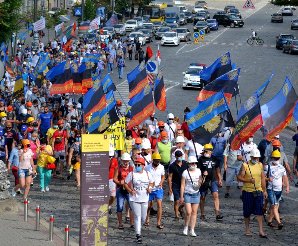 Workers in hard hats and face masks march through central Kyiv carrying blue, black and orange trade union flags.