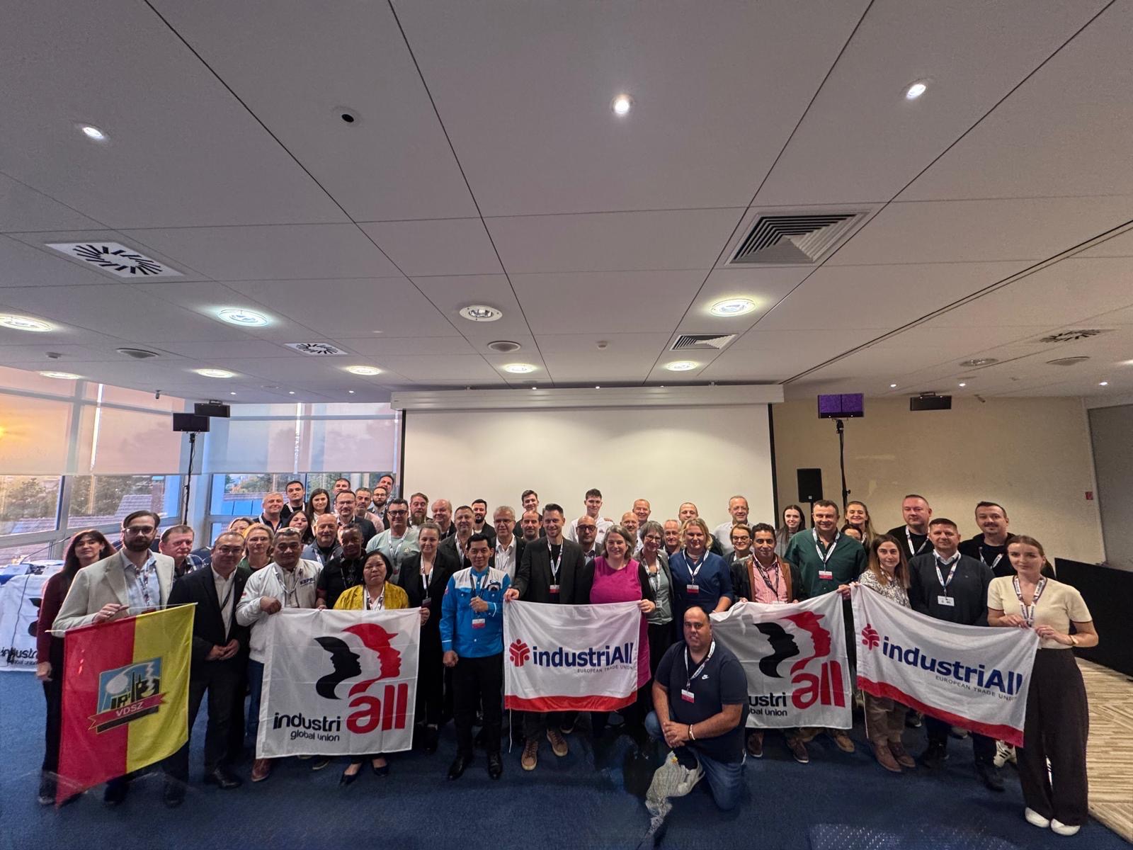 Around 60 trade unionists pose for a group photo at the battery supply chain conference in Bratislava, holding IndustriALL and industriAll Europe flags.