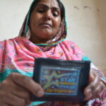 Nasri Bibi llora mientras sostiene la billetera de su hijo, que se encontró en la fábrica de Ali Enterprises donde fue muerto.