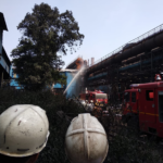 Рабочие наблюдают, как пожарные тушат пламя.